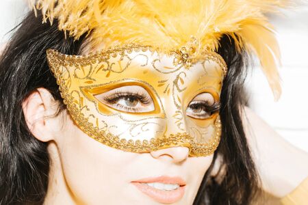 Pretty girl or beautiful woman cute, fashion, brunette model in golden, festive, carnival mask with feathers on white backgroundの写真素材