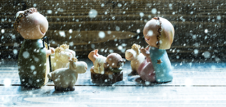 decorative celbrating Christmas and Jesus birth figurines of holy vergin Mary Josepd newborn child with few sheeps standing on wooden background under white snow and snowflakesの写真素材