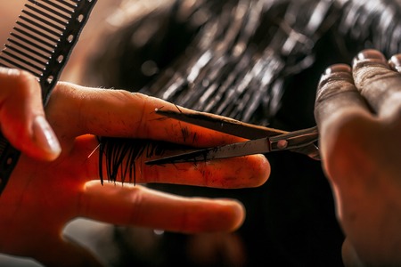 Male hands cut wet brunette hair. Professional hairdresser or barber works with scissors and comb