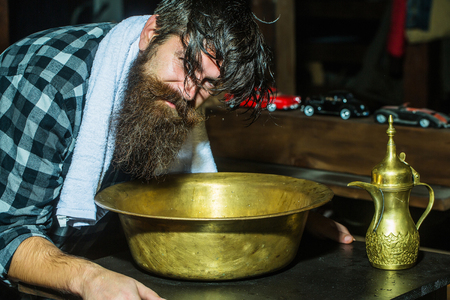 Handsome man, hipster, with beard washes hair in vintage, copper basin in barber shopの写真素材