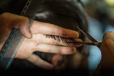 Male hands cut wet brunette hair. Professional hairdresser or barber works with scissors and combの写真素材