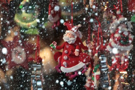 christmas toy decoration of santa claus in red coat with beard hanging on blurred background in snow and snowflakesの写真素材