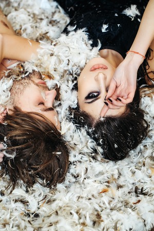 sexy christmas couple of pretty sexy woman or cute girl with long hair and fashionable makeup, handsome man with bare chest lying on white feathers as decorative new year snowflakesの写真素材