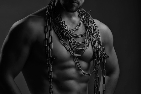 One handsome sexual strong young man with muscular body in blue jeans holding rope with hands hanging on neck and shoulders standing posing in studio black and white, horizontal pictureの写真素材
