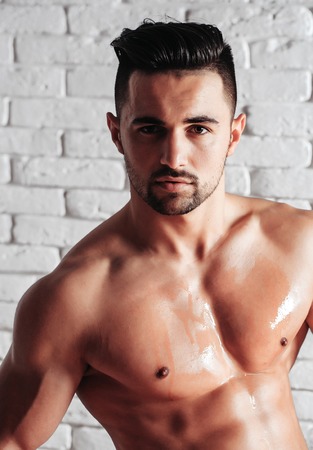 Handsome man or muscular macho, bodybuilder, with sexy, muscle torso, body, with six packs and abs poses on white brick wallの写真素材