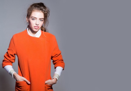 young pretty woman or cute sexy girl with long hair in fashionable orange jacket or coat, has nose...