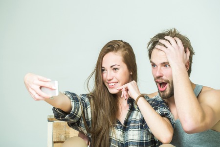 Young happy couple makes selfie on mobile phone. Pretty girl or beautiful woman, with brunette hair,...