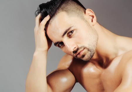 Handsome man or muscular macho, bodybuilder, with bristle, hairstyle, oily skin, sexy, muscle torso, body, with triceps, biceps poses on grey backgroundの写真素材