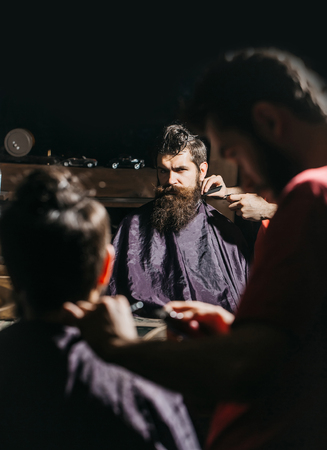Handsome bearded man, hipster, brunette with beard and moustache has haircut in hairdressing saloon or barbershop. Barber works with hair trimmer or clipperの写真素材