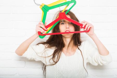 young pretty woman or cute sexy girl with long brunette hair in white fashionable sweater on brick wall background, holds shopping colorful hangersの写真素材