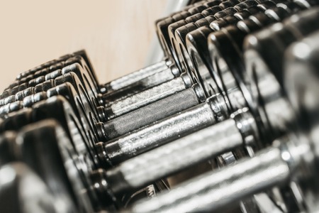 Metallic or steel heavy dumbbells, weightlifting equipment for weight training, sport, workout on stand in fitness gym on blurred grey backgroundの写真素材