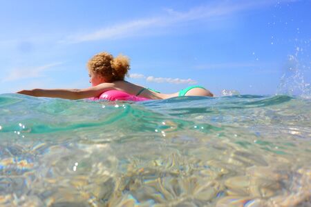 Cute young woman in bikini swims in transparent water of sea lying on rubber ring on blue sky background.の写真素材