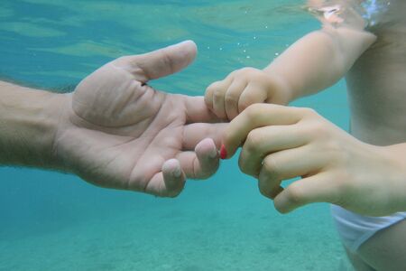 Hands of mother and child hold fathers hand under water on sea bottom.の写真素材