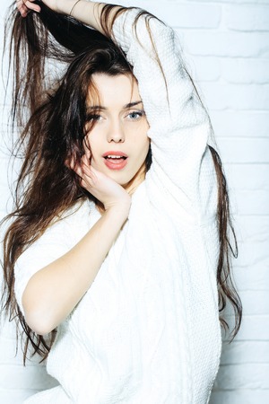 young pretty woman or cute sexy girl with long brunette hair in white fashionable sweater on brick wall backgroundの写真素材