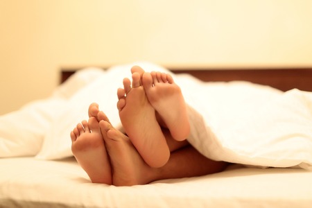 human male and female barefoot feet of woman and man couple in love laying and sleeping in white bed...
