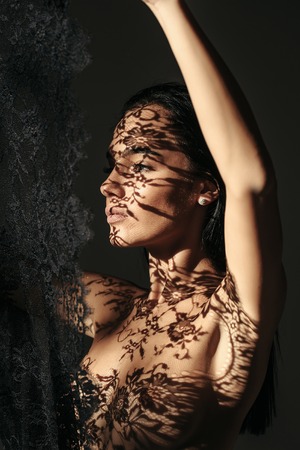 pretty naked girl or cute woman with long brunette hair holds fashionable black lace on dark background, has sexy body and bare chestの写真素材