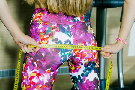 Fit woman measuring perfect shape of beautiful buttocks with tape measure after sport training,...