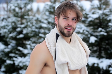 handsome bearded young man or sexy muscular guy in winter sweater outdoor in forest with fir trees with snow on natural backgroundの写真素材