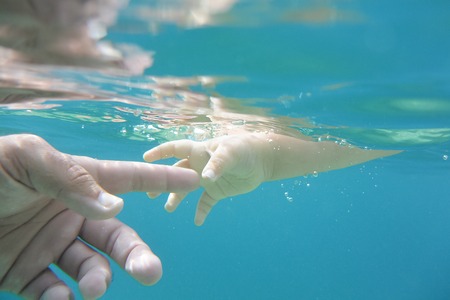 Baby hand reaches for fathers hand in clear blue water.の写真素材
