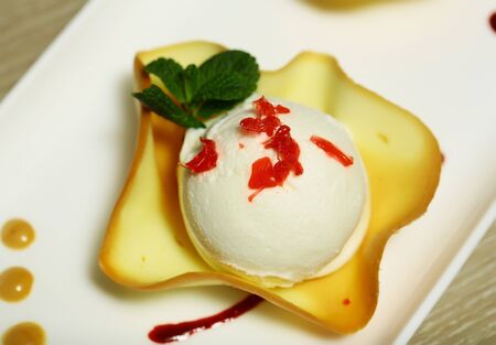 Delicious ice cream ball in wafer cup garnished with caramelized sugar candy and mint on plate on...