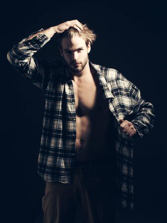 Sexy man with unbuttoned shirt touches his hair and takes his clothes off on dark backgroundの写真素材