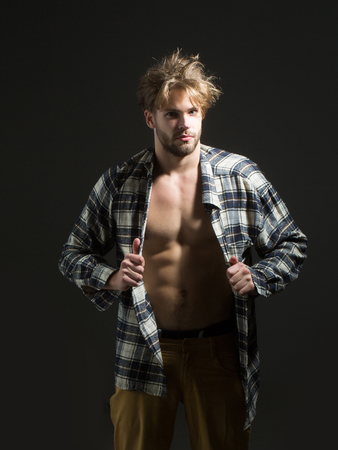 Young man in beige pants, with messy hair takes his plaid shirt off on dark backgroundの写真素材