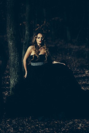 young couple of handsome man in black suit and bow with pretty sexy woman in elegant evening dress with skirt and long curly hair near tree in deep forestの写真素材