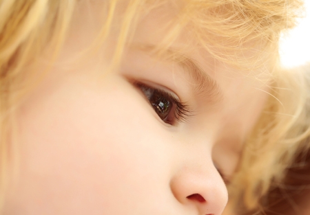 Cute brown eyes on adorable face of baby boy with cheeks and blond hair outdoors on sunny summer day...