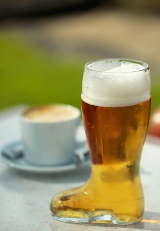 Boot shaped beer glass with frothy golden lager or ale drink on table at outdoor cafe on blurred backgroundの写真素材