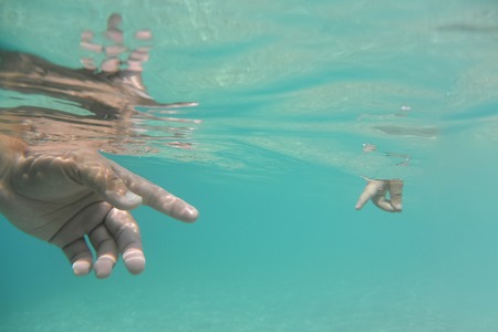 Small baby hand and big fathers hand in clear turquoise water.