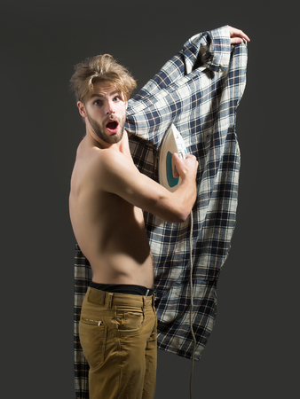 Sexy young handsome topless man irons his shirt on him with white iron on dark backgroundの写真素材