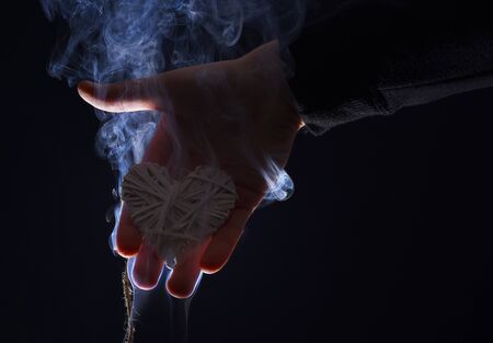 decorative straw heart in male hand as valentines day symbol of love in white smoke on black background, copy spaceの写真素材