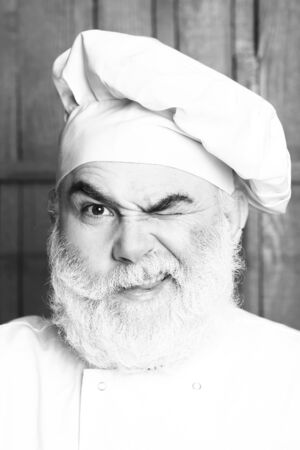 Bearded man cook in chef hat closeup in studio on wooden background, black and whiteの写真素材