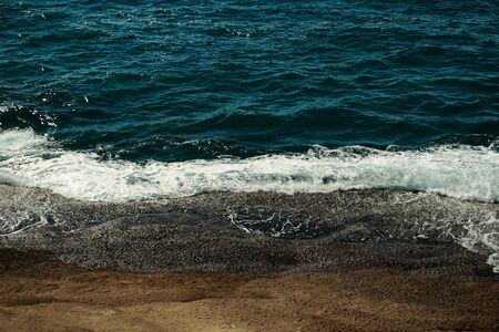 Beautiful aquamarine sea or ocean waves, surf, with white foam crash against brown stones along beach or coast from mountain on sunny day on natural backgroundの写真素材