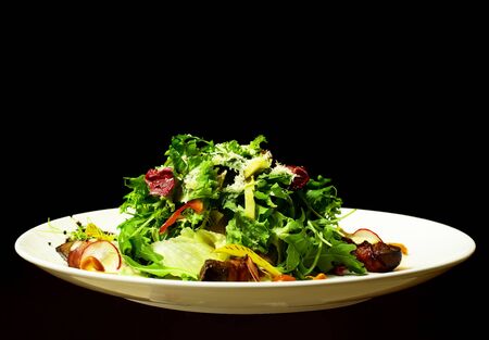 Delicious green salad mixed with roasted meat, vegetables, cheese on plate isolated on black background. Modern molecular gastronomyの写真素材
