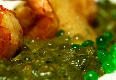 Grilled shrimps or prawns with green pea puree and caviar, vegetables, herbs with jelly texture on plate on blurred background. Modern molecular gastronomyの写真素材