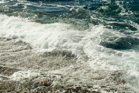 Beautiful blue sea or ocean stormy waves with white foam and ripples wash stony shore on sunny day on natural backgroundの写真素材