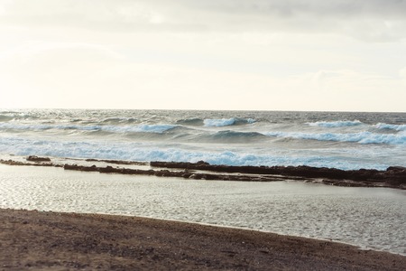 Beautiful blue waves of sea or ocean stormy water with white foam or froth splashing wash sandy beach on sunny day on natural backgroundの写真素材