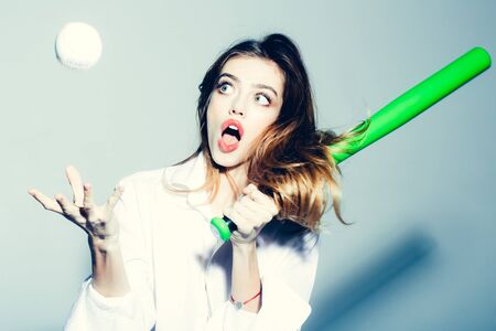 young surprised woman or pretty girl with beautiful long hair and sexy lips in fashionable white shirt holds green baseball bat or racket on grey backgroundの写真素材