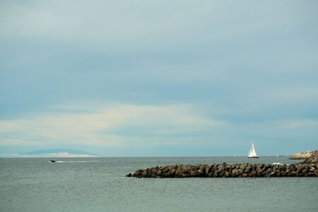 Beautiful sailing and motor boats float in calm blue sea water inshore along rocky coast outdoors on sunny summer day on sky backgroundの写真素材