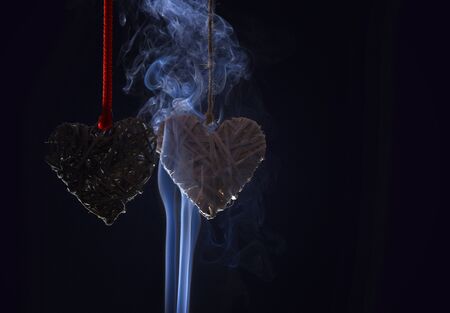 decorative straw hearts as valentines day symbol of love on red rope in white smoke on black background, copy spaceの写真素材