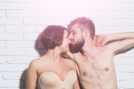 happy couple of pretty sexy woman or cute girl in bra and handsome bearded man hipster with slim bare torso and chestkiss on brick wall backgroundの写真素材
