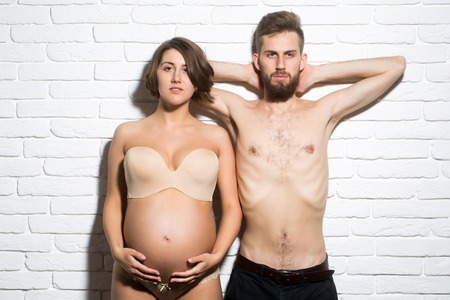 family parent couple of pretty happy sexy woman or cute pregnant girl with round belly in bra and...