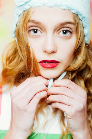 Pretty girl or beautiful woman with big eyes, red lips and blond curly hair ties cute knitted blue, beanie, hat on head on light backgroundの写真素材
