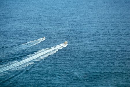 Two speed motor boats or ships travel by sea or ocean with white wakes on idyllic water surface on sunny day on blue backgroundの写真素材