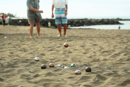 People or men play bocce sport with balls, metal and plastic boules, on natural sandy sea beach outdoors on summer day on blurred grey sand backgroundの写真素材