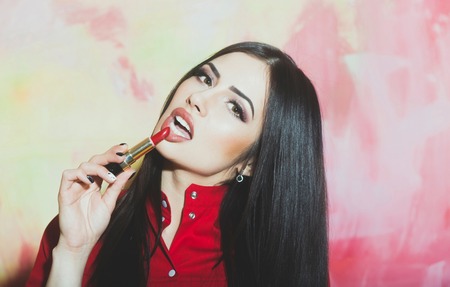 sexy cute woman or pretty girl with brunette long hair and red lipstick on lips in fashionable shirt has makeup on face on colorful backgroundの写真素材