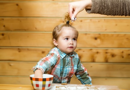 female hand and adorable small child chef or cute baby boy in fashionable chekered shirt cooking on...