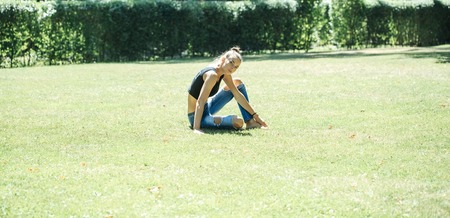 Pretty girl or beautiful fit woman in sexy black undershirt and blue jeans sits in yoga position on...