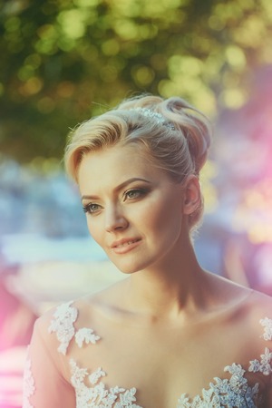 Happy pretty girl or cute woman with beautiful makeup on young face and blond hair, stylish hairstyle, smiling on sunny summer day outdoors on blurred natural backgroundの写真素材